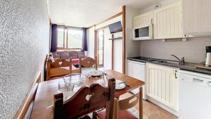 A compact kitchen with white cabinets, a microwave, and a dishwasher. There is a dining table with chairs and a window with curtains. - 2nd floor, tv, ski locker, 24m², Les Menuires (Les Menuires)