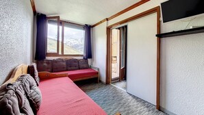 A bedroom with a bed, a sofa, a window with curtains, a door leading to a balcony, and a television on a shelf. - 2nd floor, tv, ski locker, 24m², Les Menuires (Les Menuires)
