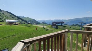 Ein malerischer Blick von einer Holzterrasse auf ein grünes Tal mit einer Seilbahn und einem Berg im Hintergrund.