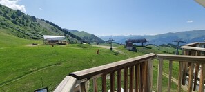 Ein malerischer Blick von einer Holzterrasse auf ein grünes Tal mit einer Seilbahn und einem Berg im Hintergrund.
