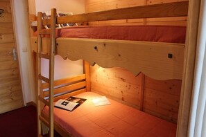 Ein Stockbett mit einer Leiter, Holzwänden und einer roten Matratze.