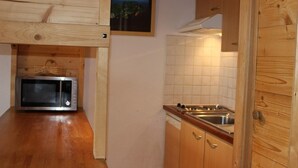 Ett kompakt kök med träskåp, en mikrovågsugn, en diskho och en kakelbeklädd vägg bakom diskbänken.