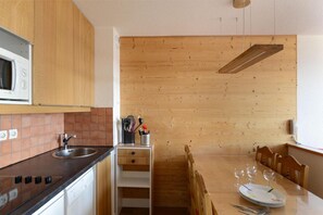 A compact kitchen with wooden cabinets, a microwave, a sink, and a dining area with a table set for four. - Ski-in/ski-out & foot of the slopes, 8th floor, view ski slopes, balcony, tv, 30m², La Plagne (La Plagne)