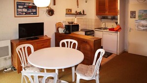 A compact kitchen with a dining area, featuring a white table, chairs, a TV, and basic appliances. - Ski-in/ski-out & foot of the slopes, 2nd floor, balcony, 28m², Les Orres (Les Orres)