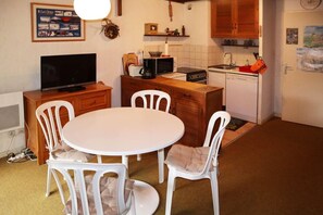 Eine kompakte Küche mit Essbereich, ausgestattet mit einem weißen Tisch, Stühlen, einem Fernseher und Grundausstattung.