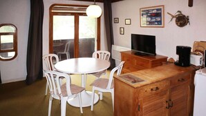 A compact kitchen with a round dining table, white chairs, a wooden cabinet, a television, and a coffee maker. - Ski-in/ski-out & foot of the slopes, 2nd floor, balcony, 28m², Les Orres (Les Orres)