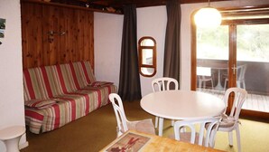 A cozy room with a striped sofa, a round table with chairs, a small wooden cabinet, and a window with curtains. - Ski-in/ski-out & foot of the slopes, 2nd floor, balcony, 28m², Les Orres (Les Orres)