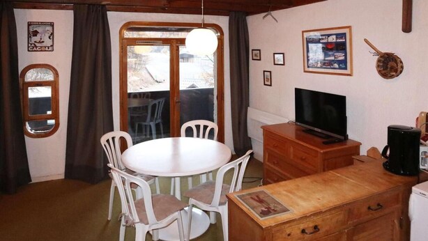 A cozy room with a round table and chairs, a television, a wooden cabinet, and a window with curtains. - Ski-in/ski-out & foot of the slopes, 2nd floor, balcony, 28m², Les Orres (Les Orres)