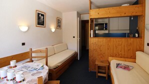 Een knus kamertje met een houten stapelbed, een kleine kitchenette, een eettafel met wat spullen en een bank.
