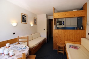 A compact room with a wooden bunk bed, a small kitchenette, a dining table with a few items, and a sofa. - 7th floor, view ski slopes, sauna, hammam, tv, 28m², Val Thorens (Val Thorens)