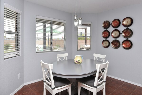 A dining area with a round table, white chairs, a hanging light fixture, and a wall-mounted decorative plate arrangement.