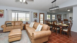 A spacious living room with a large brown leather sofa set, a dining area with wooden chairs and a table, and a kitchen visible in the background. - TMK-Spacious 4br home with pool for your comfort. EV charger available (Yuma)