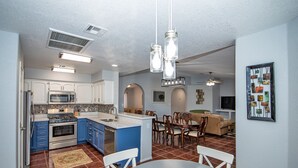 A modern kitchen with blue cabinets, a central island, and a dining area with a round table and chairs. - TMK-Spacious 4br home with pool for your comfort. EV charger available (Yuma)