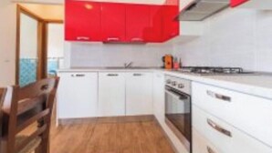 Een moderne keuken met witte kasten en rode accenten, een houten eettafel en uitzicht op de omgeving.