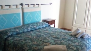 Een bed met bloemenbedrukking, een houten nachtkastje en een raam met gordijnen.