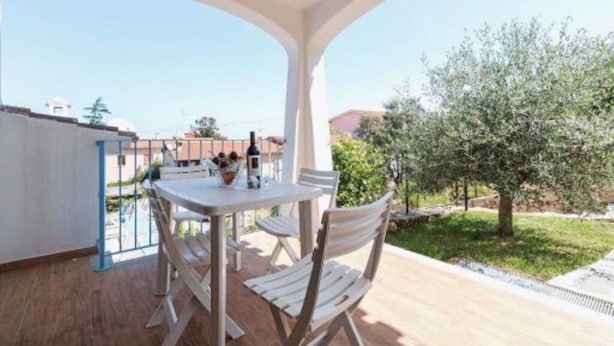 Een overdekt terras buiten, met een tafel en stoelen, en uitzicht op de omgeving, plus een boom.