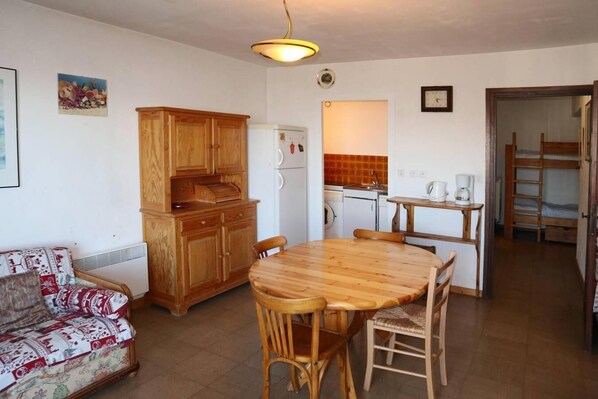A compact living space with a wooden dining table, a sofa, a kitchenette, and a bunk bed.