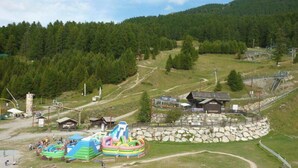Une région montagneuse comprenant un petit chalet, un parc aquatique avec des toboggans gonflables et un télésiège.