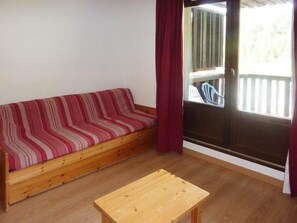 A wooden sofa with a striped cover, a wooden table, and a sliding glass door leading to an outdoor area.