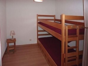 A bunk bed with a wooden frame and a red mattress. There is a small wooden nightstand with a lamp beside the bed. - Ski-in/ski-out & foot of the slopes, 5th floor, balcony, tv, 30m², Les Orres (Les Orres)