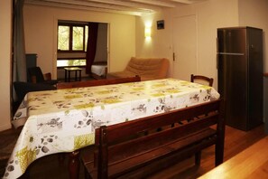 A dining area with a table set for four, a sofa, a window with curtains, and a refrigerator.