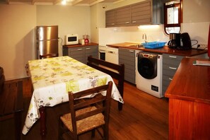 A compact kitchen with a dining table, chairs, a washing machine, a microwave, and a refrigerator.