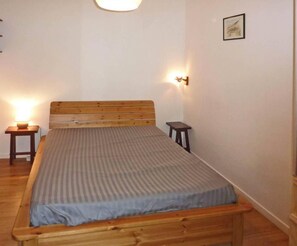 Ein Schlafzimmer mit einem hölzernen Bett, einem Nachttisch, einem kleinen Tisch und einer Wandleuchte.