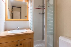 Ein Badezimmer mit einem Holzbadezimmerhocker, einem weißen Waschbecken und einer Duschkabine aus Glas.