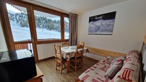 Quarto com cama, mesa com cadeiras, radiador e janela com vista para uma paisagem nevada.