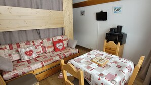 Um quarto aconchegante com sofá de madeira, uma mesinha e televisão na parede, além de um armário de madeira.