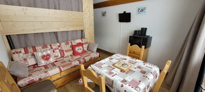 Ein gemütliches Zimmer mit einer Holzcouch, einem kleinen Tisch, einem an der Wand befestigten Fernseher und einem Holzschrank.