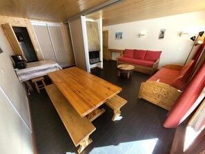 Kompakti oleskelutila, jossa on puinen ruokapöytä, penkit, punainen sohva ja pieni puinen kaappi.