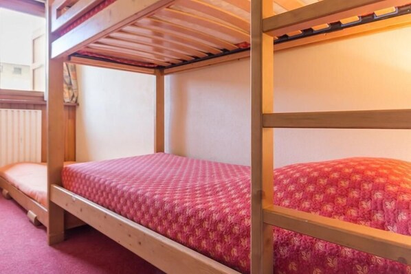 Ein Stockbett mit Holzrahmen und einer pinkfarbenen, gemusterten Decke.