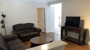 Ett vardagsrum med en brun lädersoffa, ett soffbord, en tv på ett träställ och en lampa.