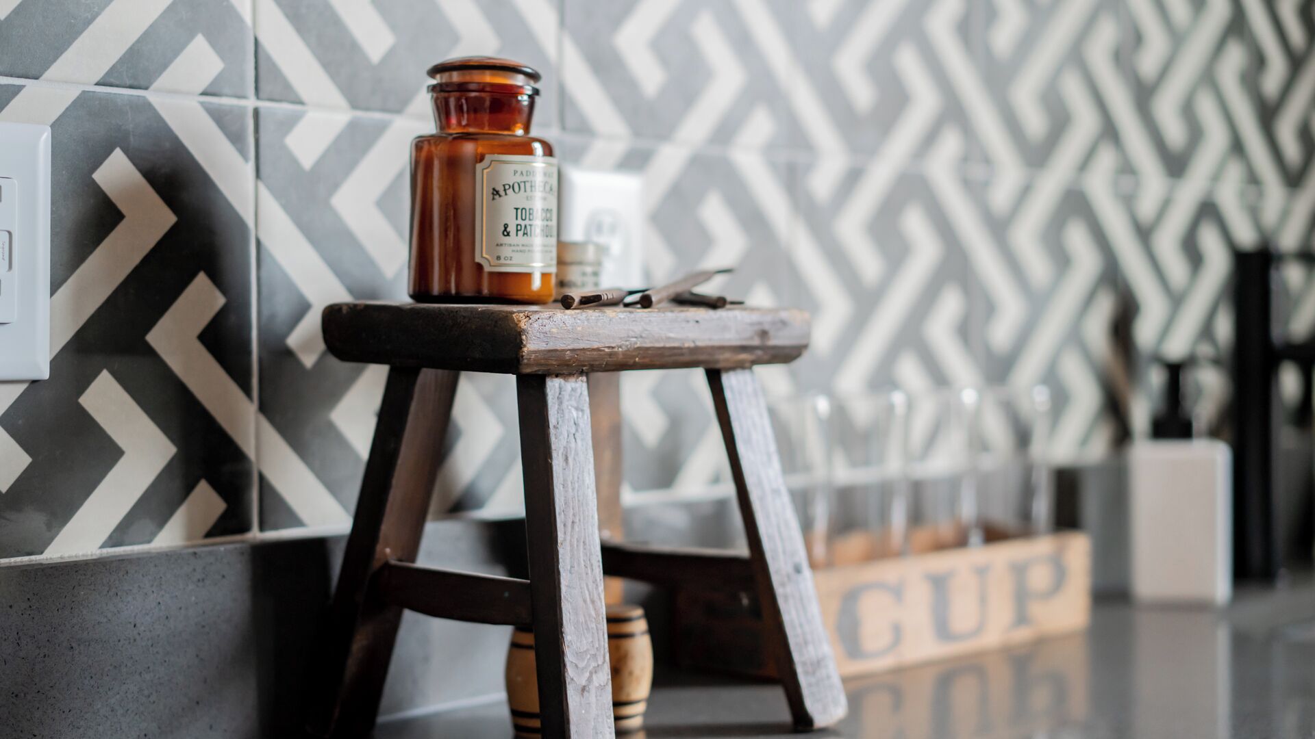 A bottle of Apothic Tobac & Patton on a wooden stool against a patterned wall.