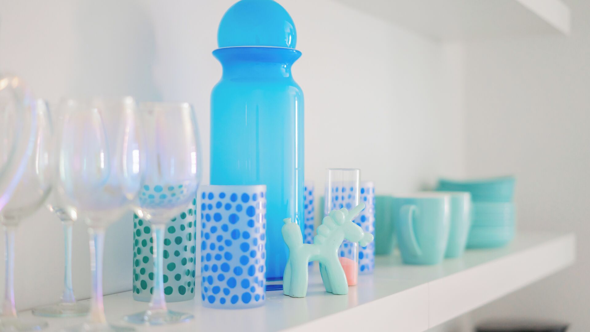 Une étagère contenant divers objets en verre et en céramique, notamment une bouteille bleue, des verres et des tasses à motifs.