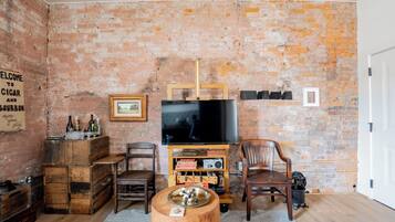 A rustic living room with exposed brick walls, a wooden TV stand, a flat-screen TV, a wooden coffee table, and a vintage radio.