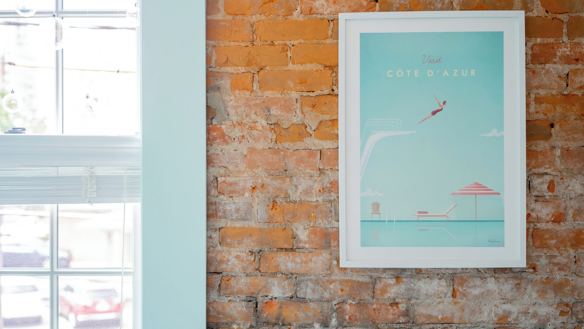 A framed poster of a swimming scene on a brick wall.