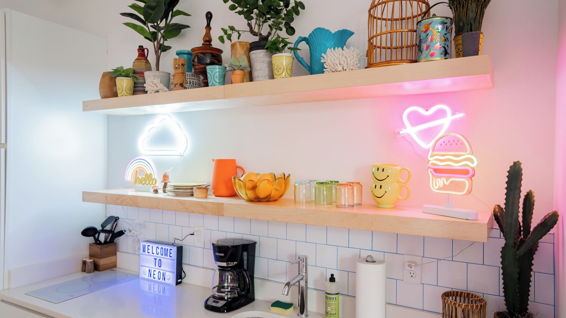 A kitchen with two illuminated shelves, a coffee maker, a sink, and a welcome sign.