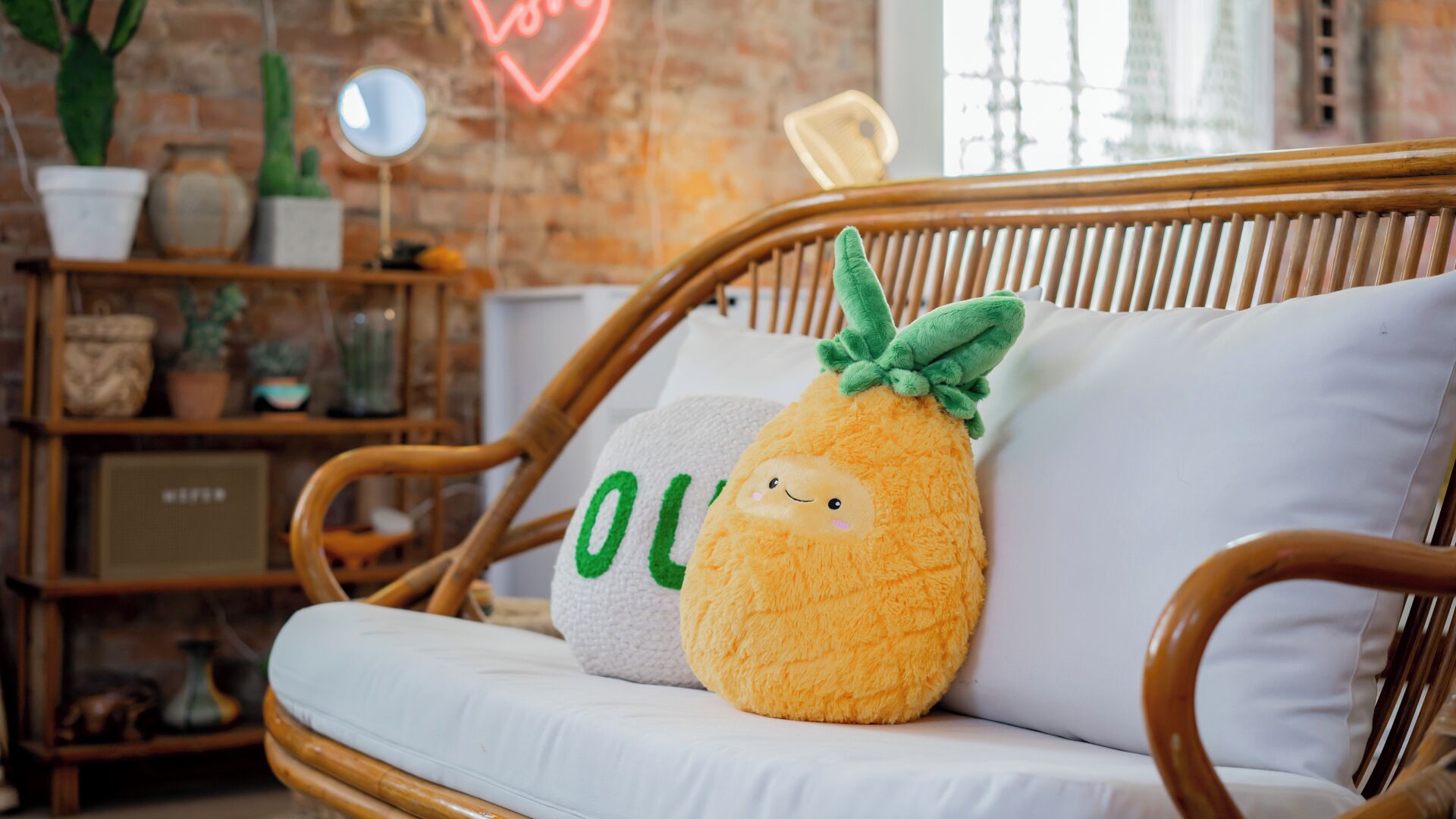A wicker sofa with a plush pineapple and a pillow with the word "LOVE" on it.