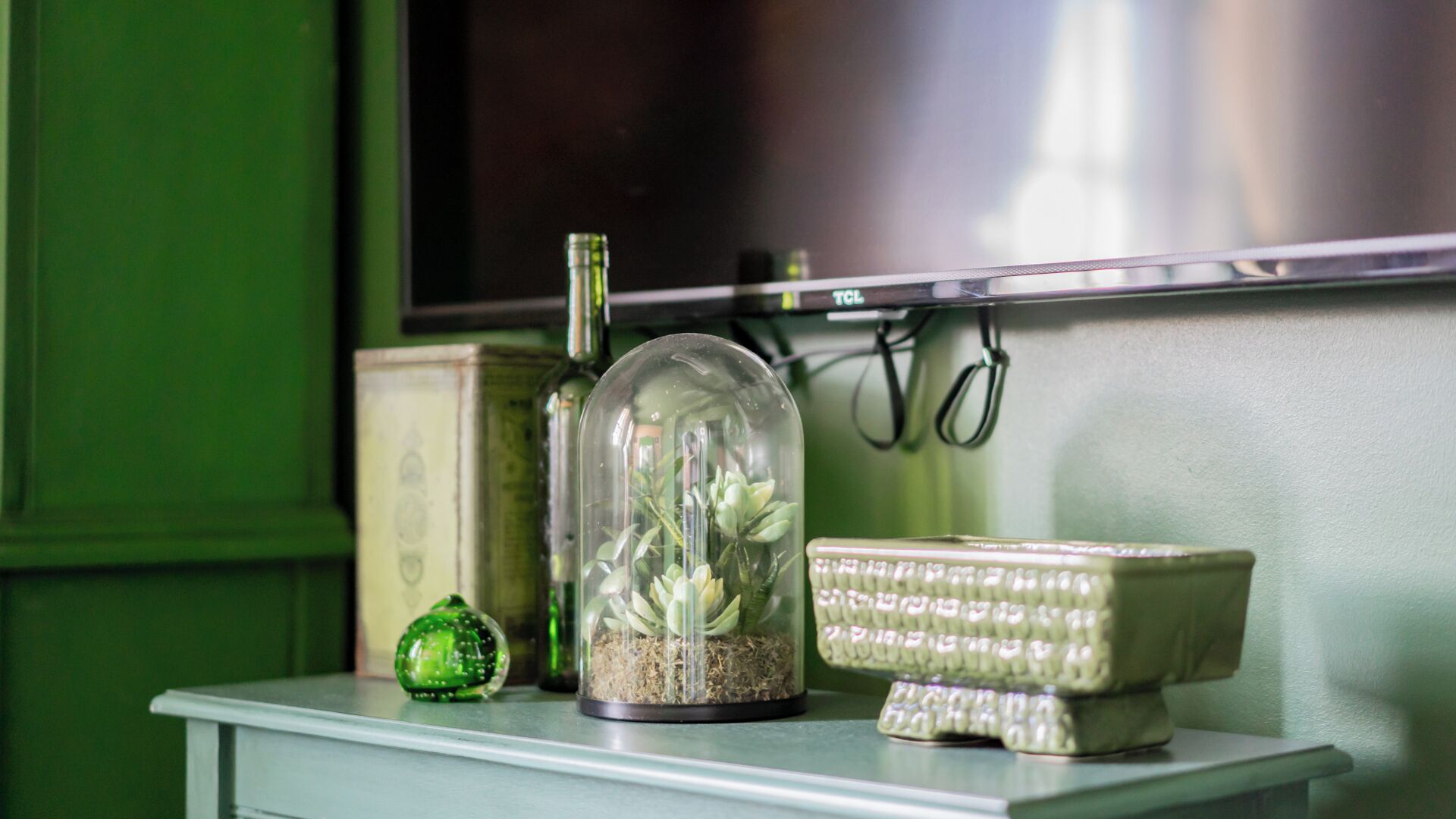 Une petite table sur laquelle sont posés un terrarium, un bol décoratif et un ornement en verre vert.