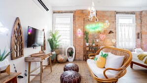 A cozy living room with a brick wall, a wicker sofa, a television, and various decorative items.