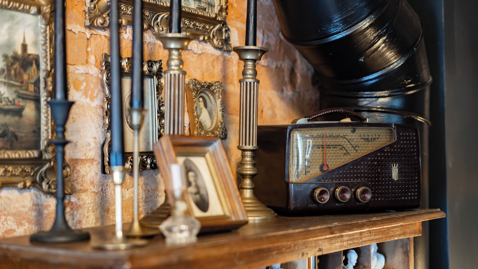 A vintage radio on a wooden shelf with ornate wall decorations and a framed picture.