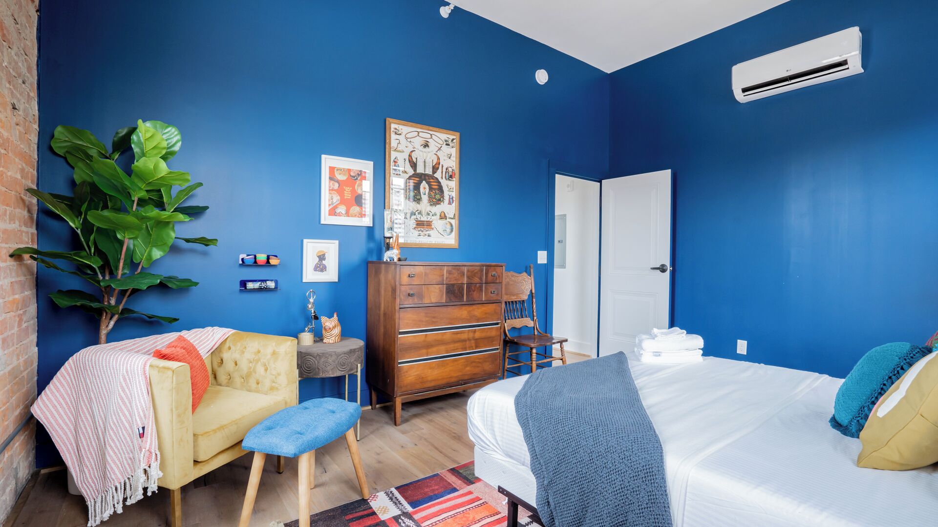 A bedroom with a blue wall, a bed, a dresser, a chair, and a plant.