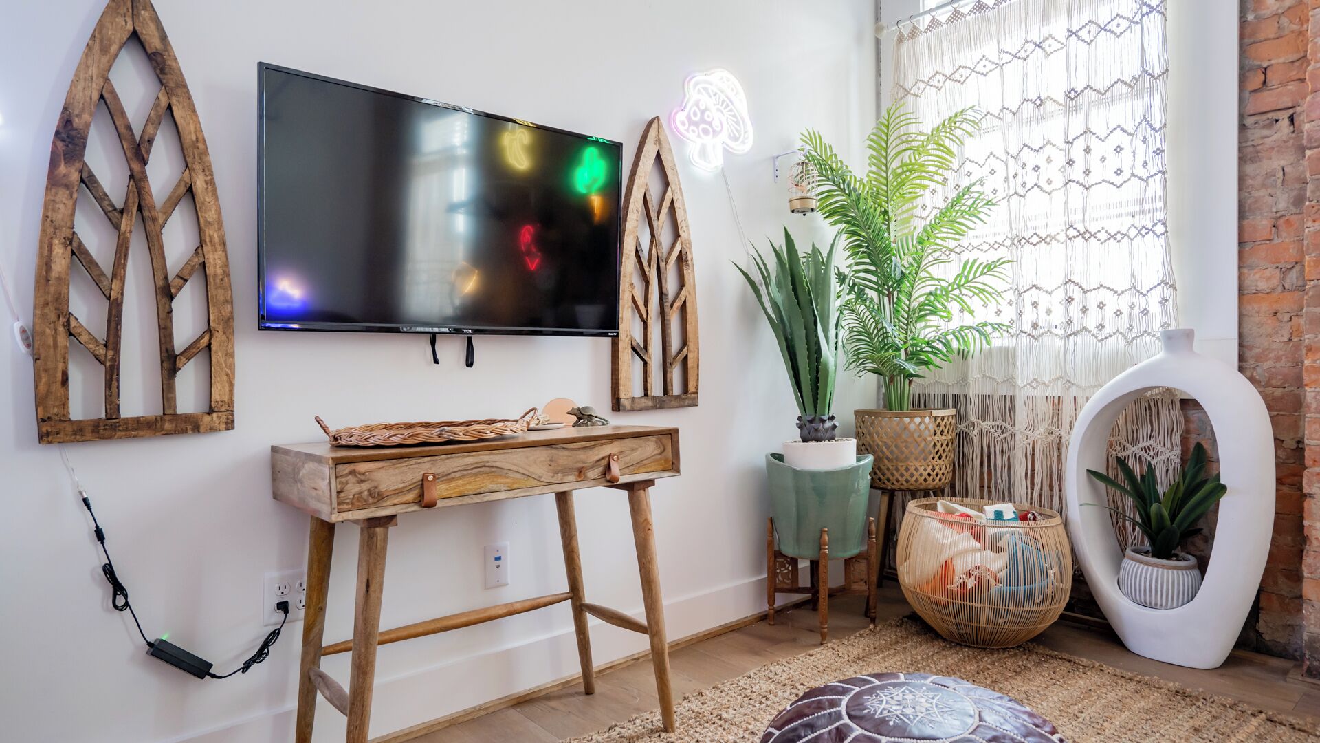 Una sala de estar moderna con un televisor de pantalla plana montado en la pared, muebles de madera, una planta en maceta y una cortina de macramé.