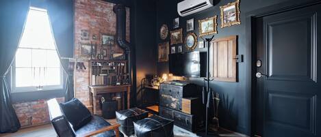 A room with a brick wall, a black leather chair, a vintage trunk, and a large black door.