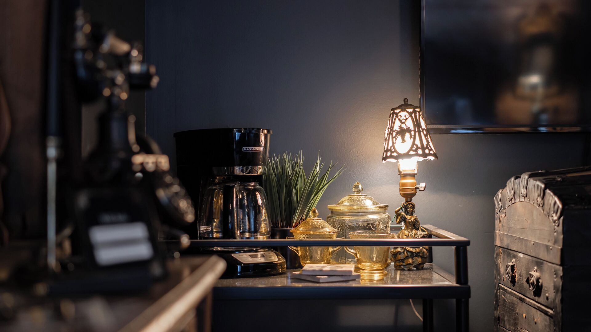 Uma mesa com cafeteira, luminária e objetos decorativos.
