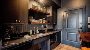 A modern kitchen with dark cabinetry, a black countertop, and a wooden chair.