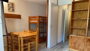 A room with a wooden dining table and chairs, a bunk bed, and a wooden wardrobe.
