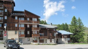 A multi-story wooden building with balconies, a parking lot, and a clear sky.